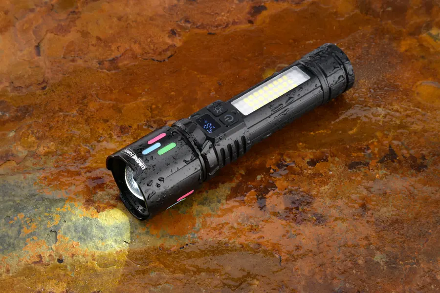 The Lumen Force flashlight resting on a wet, rust-colored metal surface, beaded with water droplets and its beam glowing, showing its IP44 water resistance.